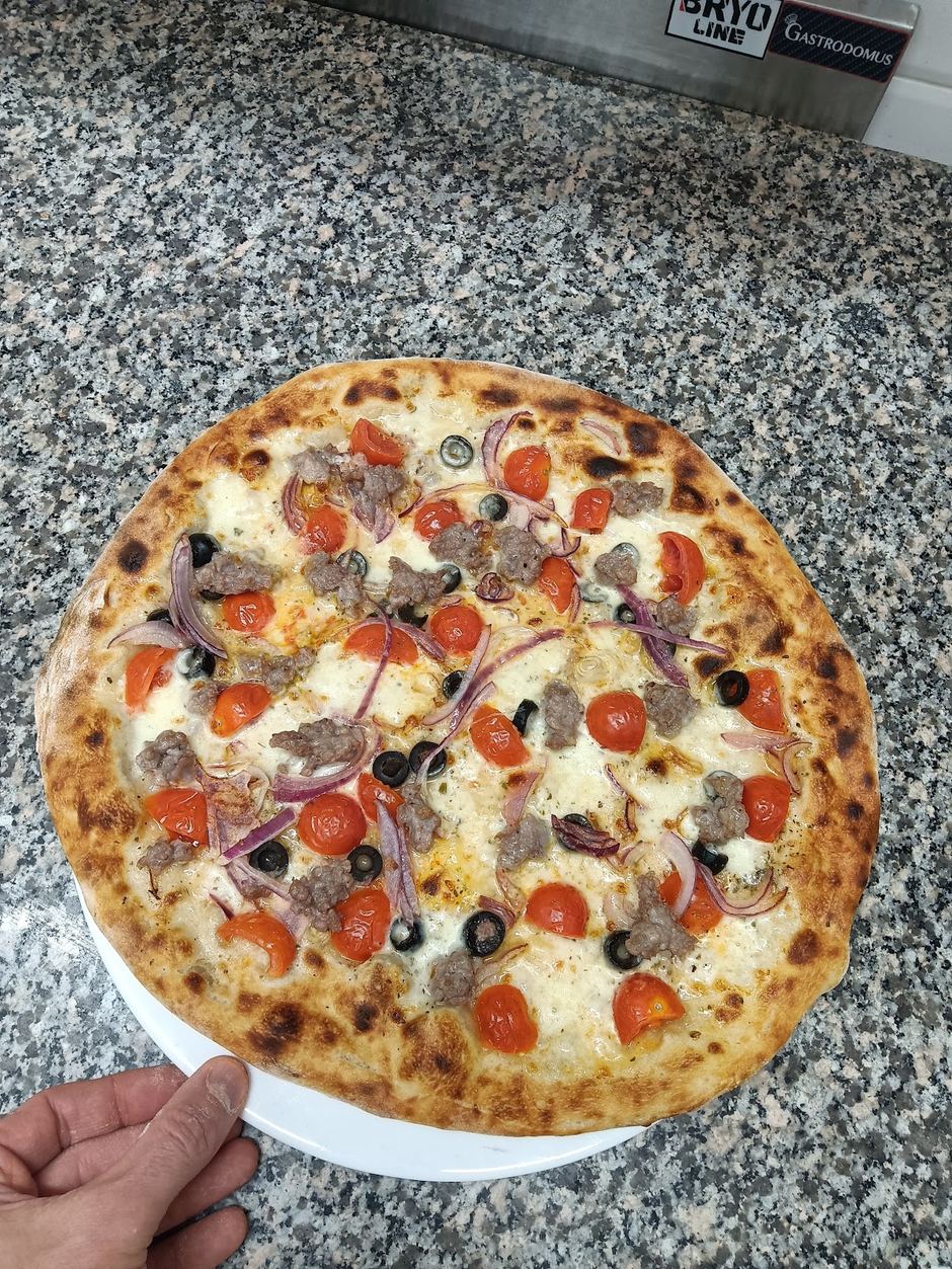 Pizza appena sfornata con pomodorini, salsiccia, olive e cipolla di Tropea